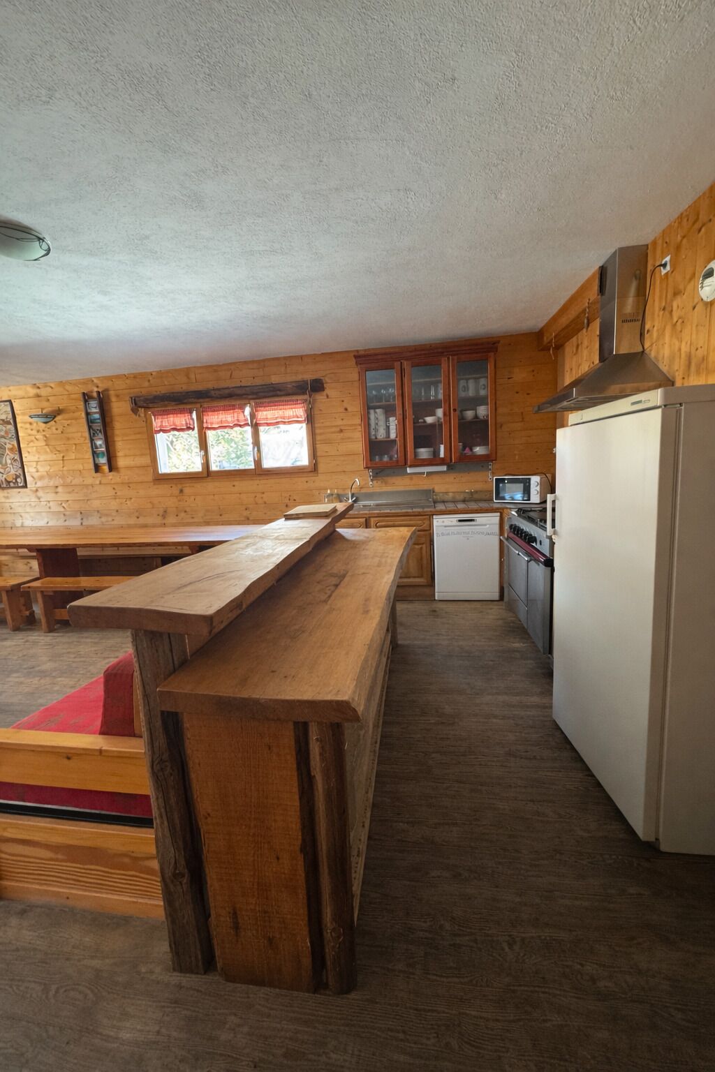 Een keuken met houten kastjes, een houten eettafel, een witte koelkast en een magnetron.