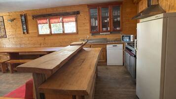 Een keuken met houten kastjes, een houten eettafel, een witte koelkast en een magnetron.