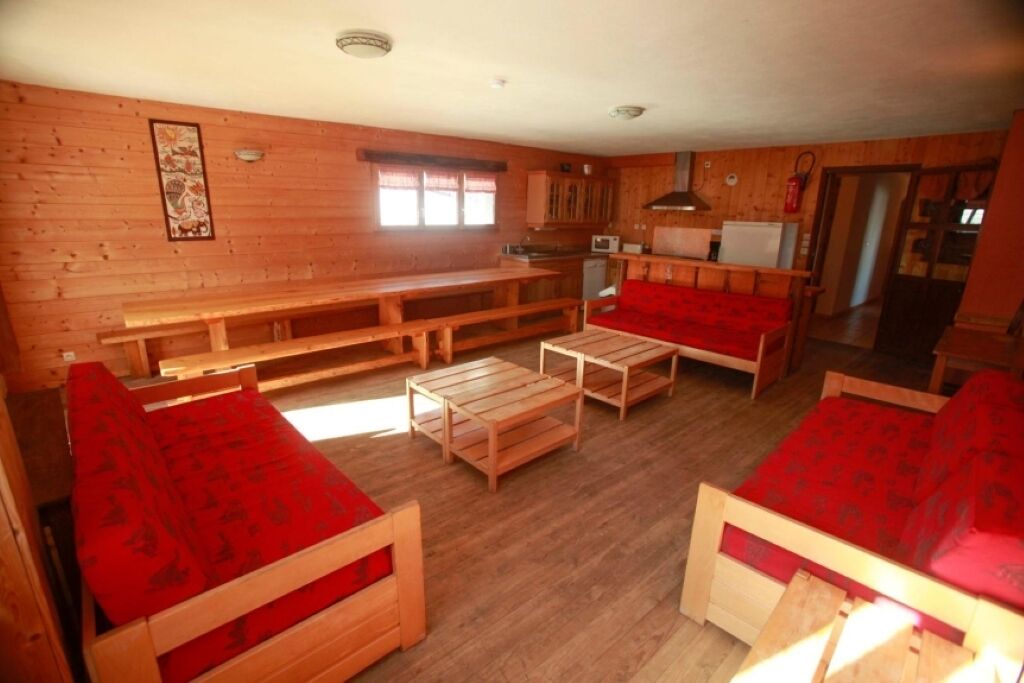 Un intérieur en bois comprenant un coin repas, une cuisine et un salon avec des meubles recouverts d’un tissu rouge.