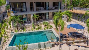 Ein modernes, zweistöckiges Gebäude mit Pool, Außenbereich und tropischer Bepflanzung.