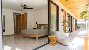 Ein modernes Schlafzimmer mit einem Bett, einem Deckenventilator und einer großen Schiebetür, die zu einem Balkon führt.