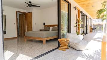 Une chambre à coucher moderne, équipée d’un lit, d’un ventilateur de plafond et d’une grande porte-fenêtre coulissante donnant sur un balcon.