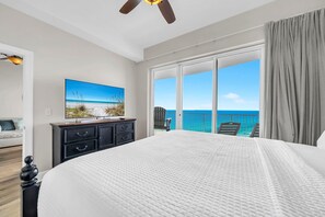 Ein Schlafzimmer mit einem großen Bett, einem Fernseher, einem Deckenventilator und einem Balkon mit Meerblick.