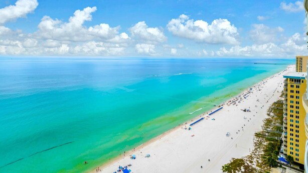 A beach with clear turquoise water, a sandy shore, and a tall building on the right. - Ocean Villa Penthouse 2306 (Panama City Beach)
