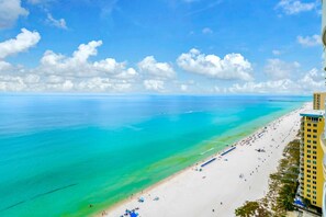 A beach with clear turquoise water, a sandy shore, and a tall building on the right. - Ocean Villa Penthouse 2306 (Panama City Beach)