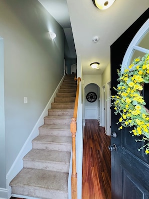 A carpeted staircase with wooden handrails, a black door with a yellow flower arrangement, and a hallway with a light fixture. - 5 miles from Augusta National. MASTERS (Augusta)