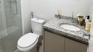 Een moderne badkamer met een douchecabine van glas, een toilet, een wastafel met een granieten blad en een spiegel met een zwarte lijst.