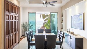 A dining area with a view of the ocean, a ceiling fan, and a large wooden wardrobe. - Beachfront with pier and saltwater pool for 14 ppl 4 bedrooms (Cozumel)