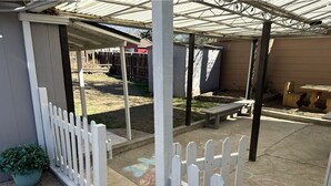 A covered patio area with a white picket fence, a concrete floor, and a wooden bench. - Elmira 1-bedroom guesthouse in beautiful Aurora (Aurora)