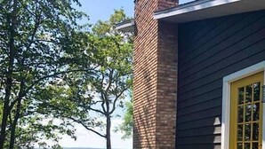 Ett hus med en tegelbeklädd skorsten, en gul dörr och utsikt över en sjö eller ett annat vattendrag.