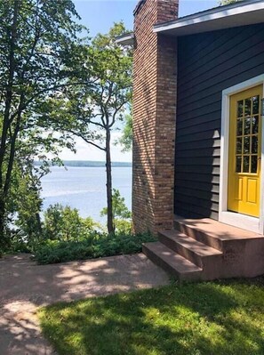 Ein Haus mit einem Ziegelkamin, einer gelben Tür und Blick auf ein Gewässer.
