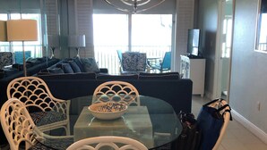 Ein Essbereich mit einem Glastisch, weißen Korbstühlen, einer Chandelierleuchtre und Blick ins Freie.