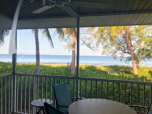 A covered outdoor area with a table and chairs, a view of the sea, and a palm tree. - No Place Like Captiva 2 Bedroom Condo Beautiful Views Pool Beach (Captiva)