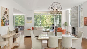 A modern living room with a dining area, large windows, and a fireplace. - Luxury 6-Bedroom Gated Estate on 5 Acres with Pool, Tennis, Gym & Privacy (Bridgehampton)