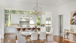 A modern kitchen with white cabinets, a large island, and a dining area with chairs. - Luxury 6-Bedroom Gated Estate on 5 Acres with Pool, Tennis, Gym & Privacy (Bridgehampton)