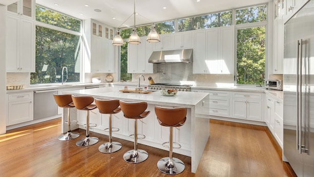 A modern kitchen with a central island, bar stools, and large windows. - Luxury 6-Bedroom Gated Estate on 5 Acres with Pool, Tennis, Gym & Privacy (Bridgehampton)