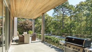 An outdoor patio with a grill, seating area, and a view of trees. - Luxury 6-Bedroom Gated Estate on 5 Acres with Pool, Tennis, Gym & Privacy (Bridgehampton)