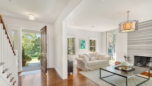 A spacious living room with hardwood floors, a white sofa, a glass coffee table, and a fireplace. - Luxury 6-Bedroom Gated Estate on 5 Acres with Pool, Tennis, Gym & Privacy (Bridgehampton)