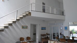 Un intérieur spacieux avec un escalier menant à un balcon, des meubles en osier et un coin repas.