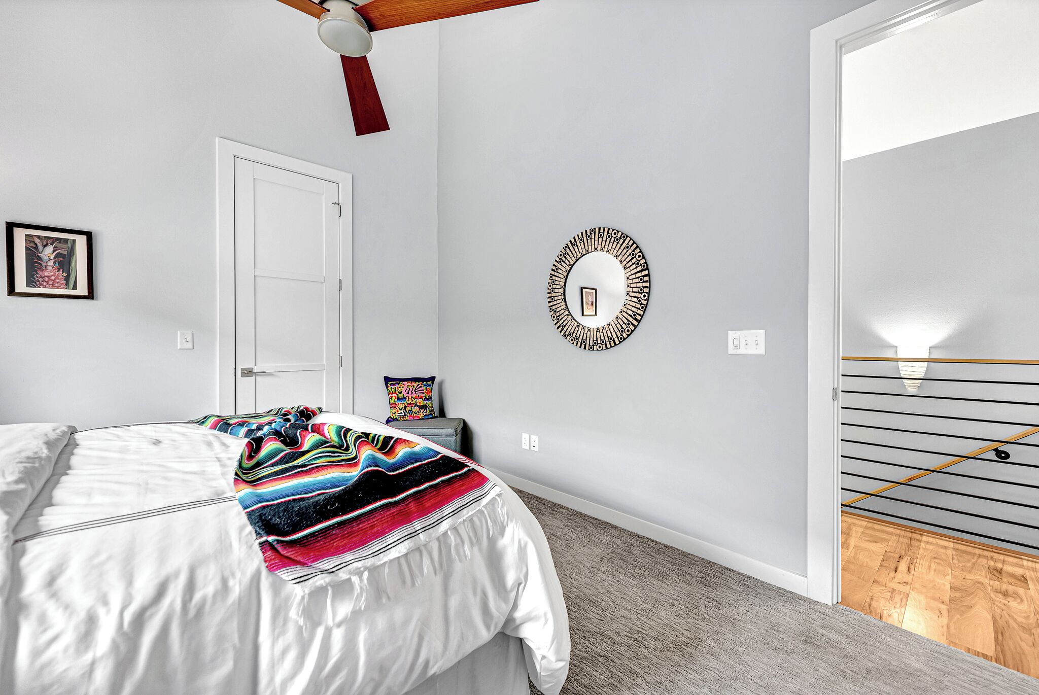Une chambre à coucher avec un lit, une couverture colorée, une horloge murale, une porte et un luminaire.