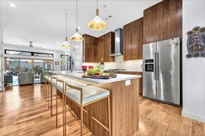 A modern kitchen with wooden cabinets, stainless steel appliances, and a bar area with stools. - Casa La Rosa (Bentonville)