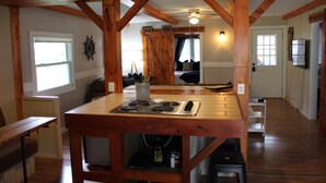 A wooden kitchen with a stove, a dining table, and a bench. - Charming 2-bedroom Lake Cottage (Durhamville)