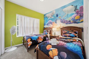 Une chambre avec deux lits, un ventilateur, une fenêtre et une fresque murale représentant la vie marine sous-marine.