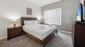 A bedroom with a bed, nightstands, a dresser, a television, a window with blinds, and a framed picture on the wall. - Sunshine Stay Near Disney  2BR  Walk to Pool (Kissimmee)