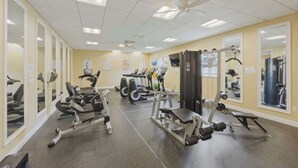 A gym with cardio machines, weightlifting equipment, and mirrors on the walls. - Sunshine Stay Near Disney  2BR  Walk to Pool (Kissimmee)
