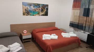 Una camera d'albergo con un letto, un comodino, un tavolino da notte, un quadro appeso al muro e una finestra con tende.