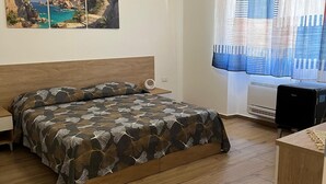 Ένα υπνοδωμάτιο με ένα κρεβάτι, ένα γραφείο, ένα παράθυρο με κουρτίνες και ένα κλιματιστικό τοποθετημένο στον τοίχο.