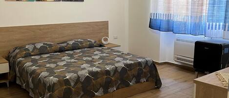 Une chambre à coucher comprenant un lit, un bureau, une fenêtre avec des rideaux et un climatiseur fixé au mur.