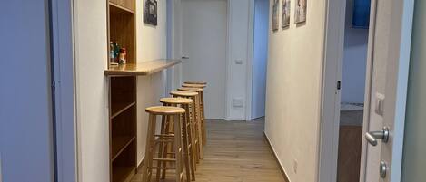 A hallway with wooden flooring, a row of stools, a wooden cabinet, and a door leading to another room.