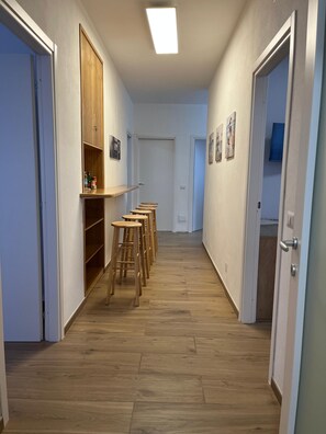 Een gang met houten vloeren, een rij krukken, een houten kast en een deur naar een andere kamer.