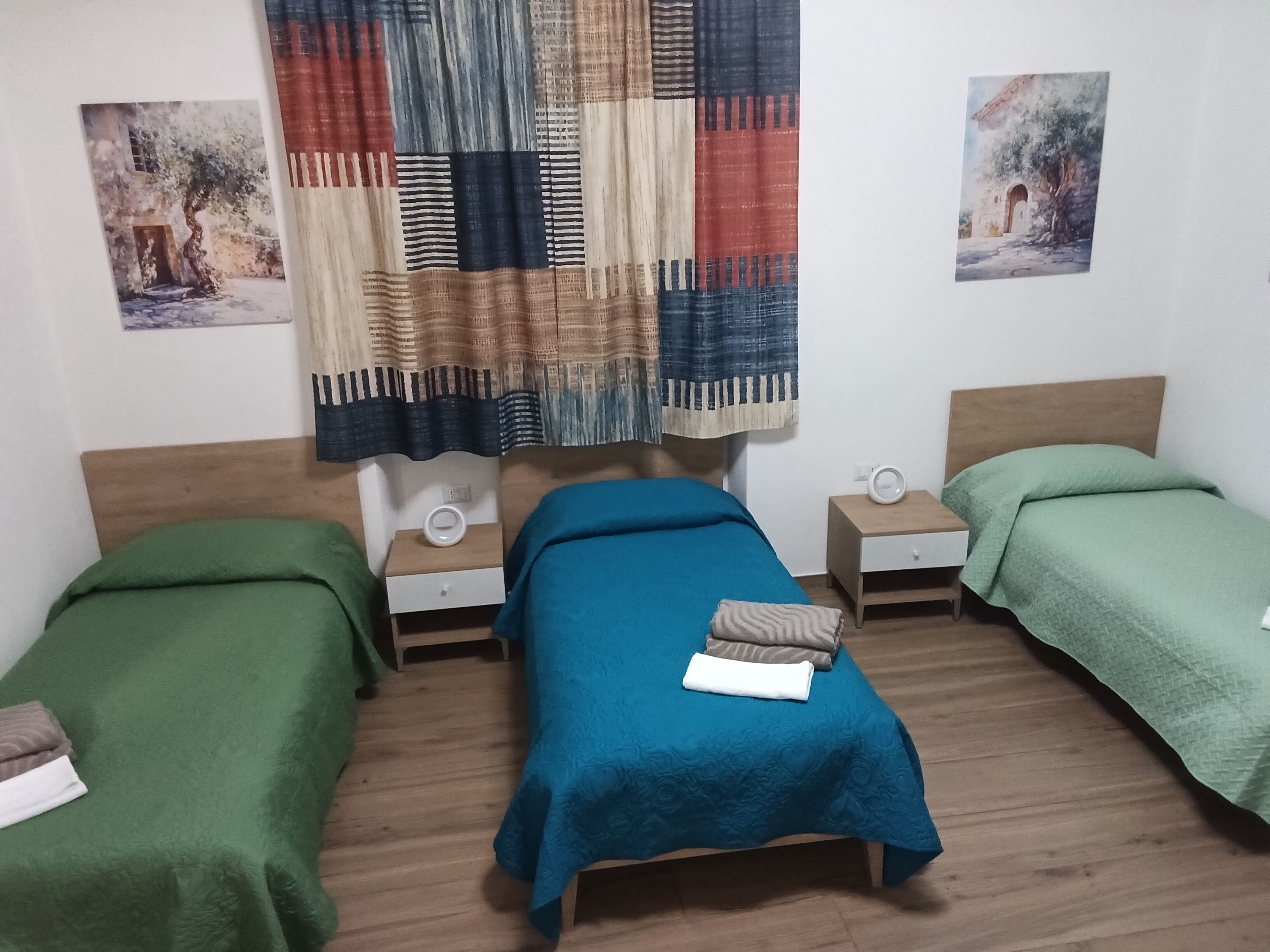 Una habitación con dos camas individuales, un cabecero de madera, una mesita de noche con lámpara y una cortina con diseño de patchwork.