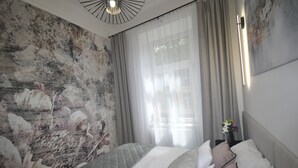 A bedroom with a bed, curtains, a wall mural, and a nightstand with a vase. - Wesoła Station by JoApart - Old Town (Kraków)