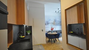 A modern kitchen with a black countertop, wooden cabinets, and a dining area with a round table and blue chairs. - Wesoła Station by JoApart - Old Town (Kraków)