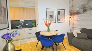 A modern living room with a round table, blue chairs, a grey sofa, and a large abstract painting on the wall. - Wesoła Station by JoApart - Old Town (Kraków)