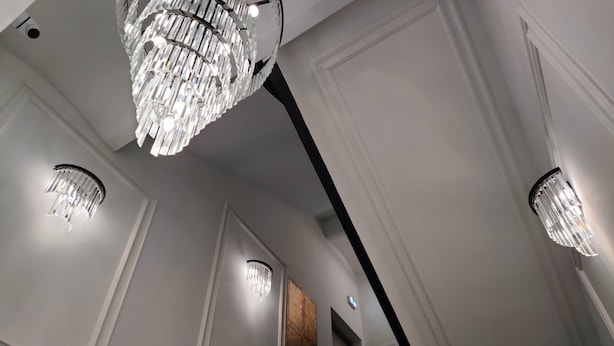 A staircase with a black railing, white walls, and a chandelier. - Wesoła Station by JoApart - Old Town (Kraków)
