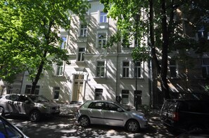 Un edificio de varios pisos con coches aparcados, árboles y una entrada visible.