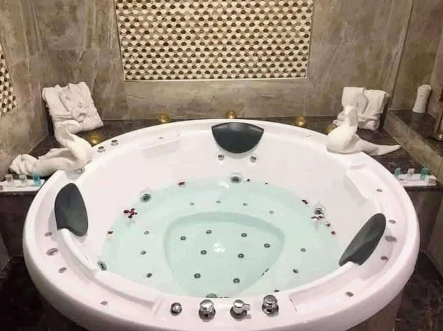 A round hot tub with jets, a textured wall behind it, and a towel rack to the left.