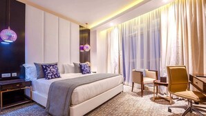 Une chambre d’hôtel comprenant un lit, une table de chevet, une chaise, un bureau et des rideaux.