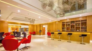 Un hall d’hôtel moderne avec un bar, des fauteuils rouges et gris et un sol ciré.