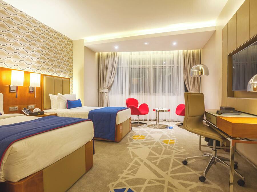 Habitación de hotel con dos camas, un escritorio, una silla, un televisor y una ventana con cortinas.