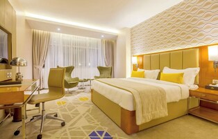 Habitación de hotel con cama, escritorio, silla y un gran ventanal con cortinas.