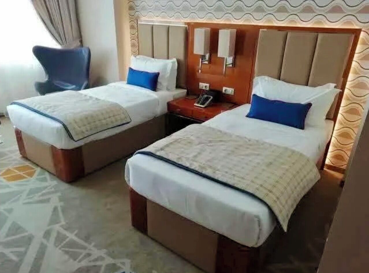 Habitación de hotel con dos camas, una mesita de noche, una silla y una alfombra estampada.