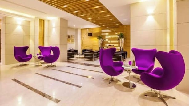 Un hall d’entrée avec des fauteuils violets, un comptoir d’accueil et un plafond en bois.