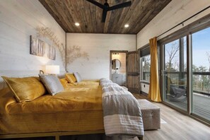 Ein Schlafzimmer mit einem großen Bett, einer Bank, einem Spiegel und Blick durch ein großes Fenster.