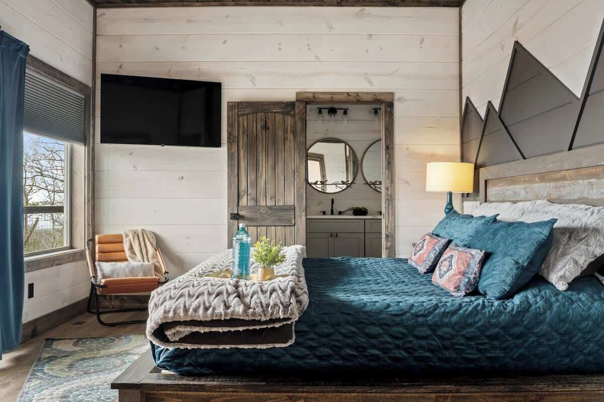 A bedroom with a bed, a chair, a mirror, and a television.