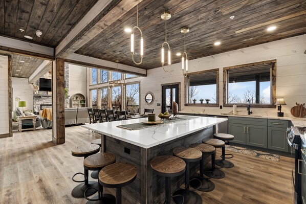 A spacious kitchen with a large island, wooden bar stools, and pendant lighting.